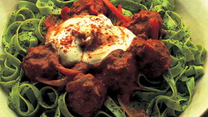 a picture of cooked Meatballs Braised in Goulash Sauce sitting on green noodles in a yellow bowl