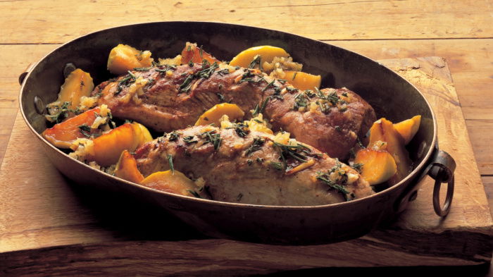 an oval casserole dish of roast pork, with apples on a wooden board