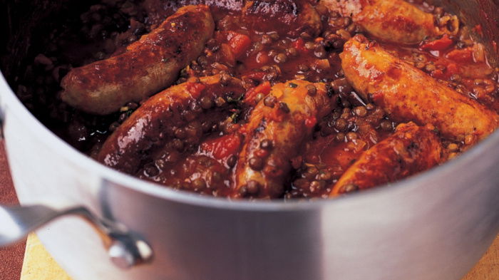 a pan of cooked sausages and puy lentils on a wooden board