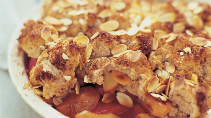 cooked plum and almond cobbler with pastry topping and flaked almonds in a white bowl
