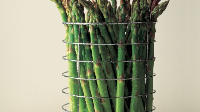 a picture of fresh asparagus in a wire container sitting on a marble surface
