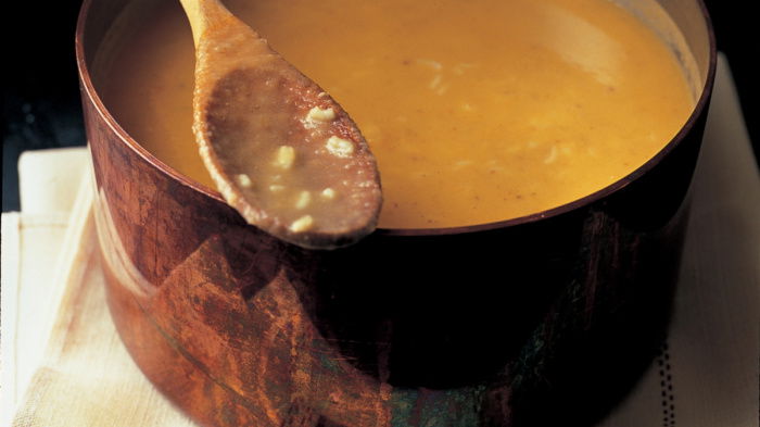 A copper saucepan full of cooked mulligatawny soup with a wooden spoon resting on the rim