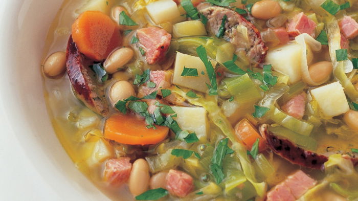 A white bowl of soup showing diced vegetables and frankfurter