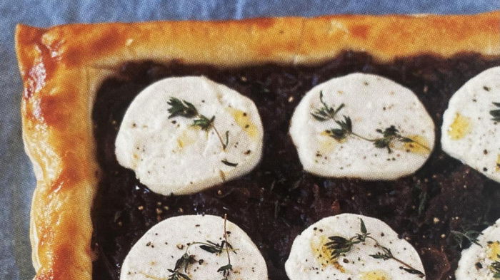 A sheet of cooked puff pastry with a layer of red onion and nine rounds of goats' cheese and some fresh thyme and oil drizzled over the top