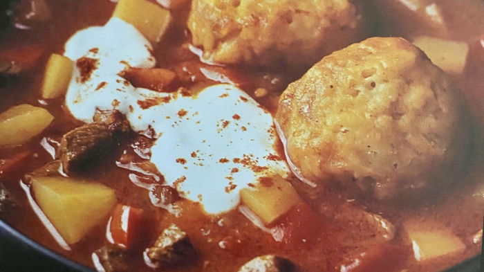 A brown soup bowl with goulash soup and dumplings on the top