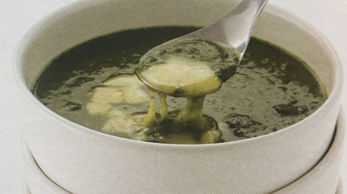 a picture of spinach soup and melted cheese in a white soup bowl with spoon