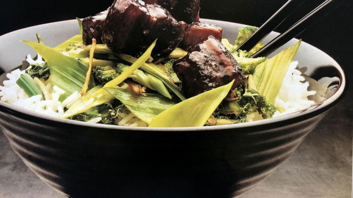 Cooked pork and stirefry greens in a brown bowl with two chopsticks resting on the side