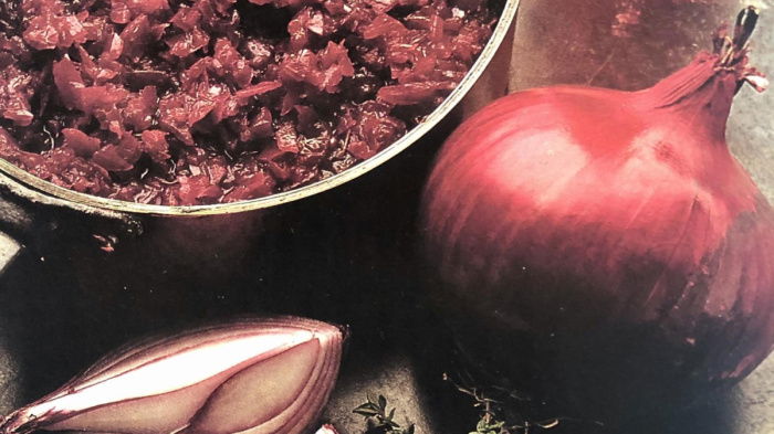 a pan of red onion marmalade with a whole red onion and a quartered red onion and a bunch of thyme on the side