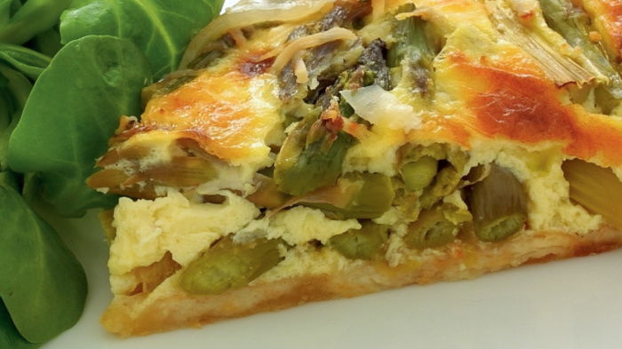 a picture of a slice of asparagus tart with salad leaves on a white plate