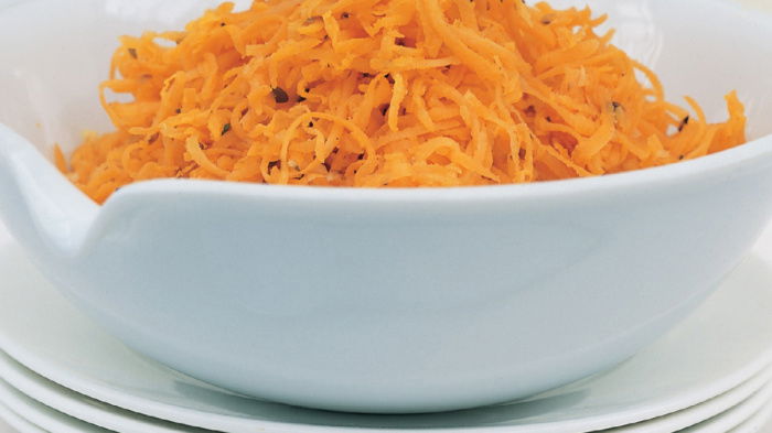 Grated carrot in a white bowl on top of a stack of four white plates