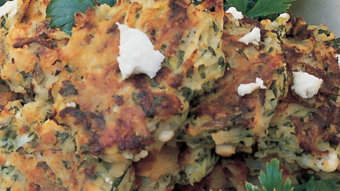 A white bowl of cooked potato cakes with feta cheese and parsley scattered on top