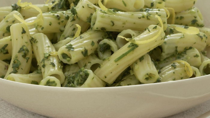 A white bowl of cooked pasta with flecks of herbs and lemon zest