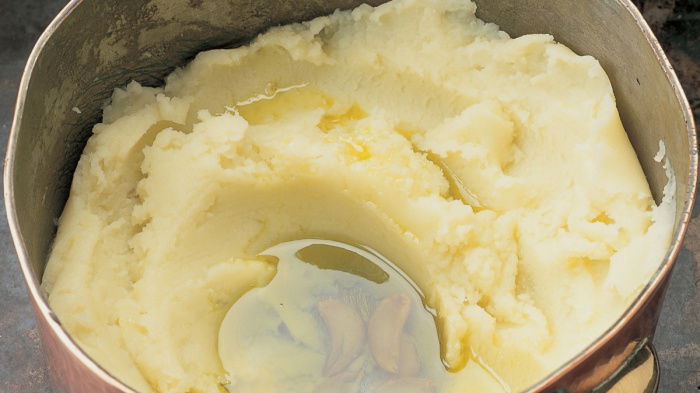 A copper pan of lovely mashed potato and cloves of garlic in a pool of olive oil