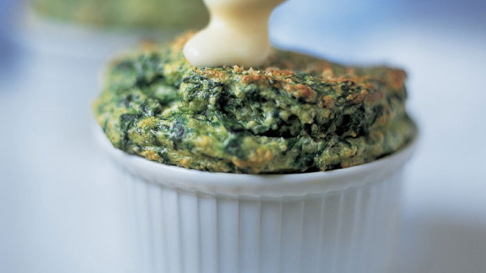 a ramekin with cooked spinach souffle and a spoon dripping sauce on top