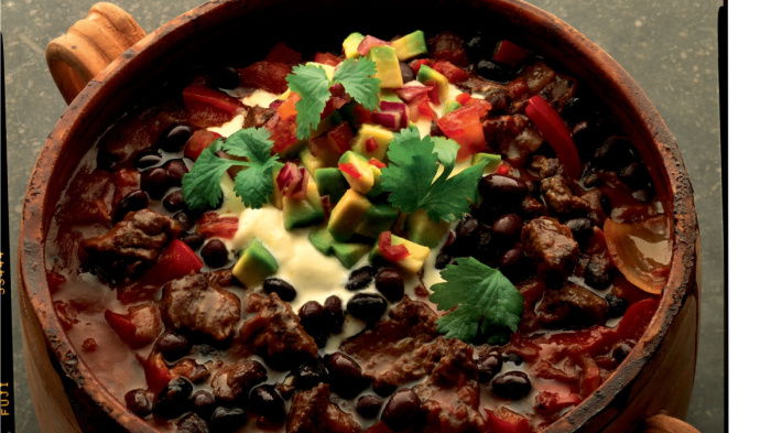 An earthenware bowl containing chilli beef with creme fraiche and avocado salsa on the top and a little parsley garnish