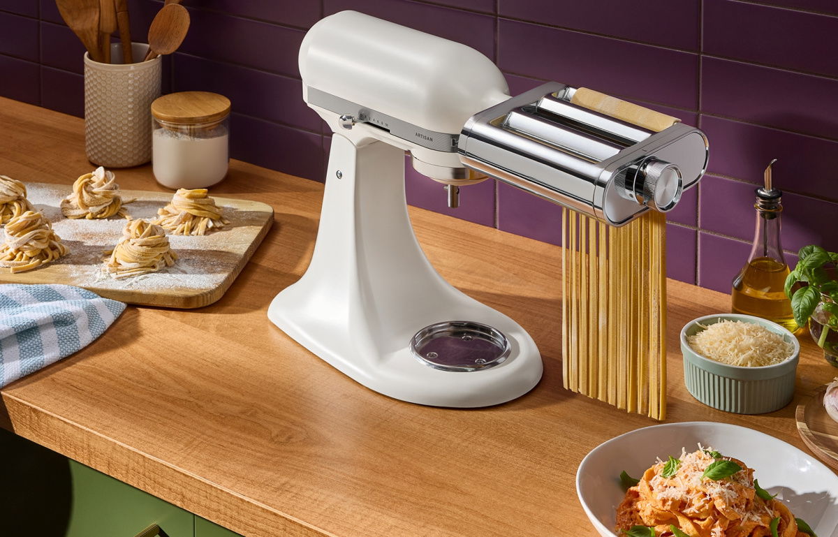a white ktchenaid stand mixer with pasta attachment sitting on a wooden counter top