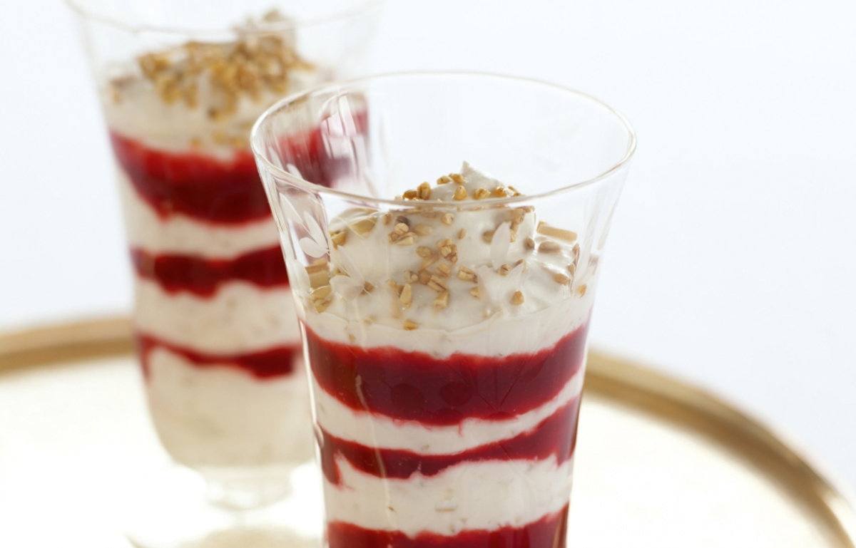 Two tall dessert glasses filled with layers of cream and raspberry sauce on a gold tray with two spoons on the side