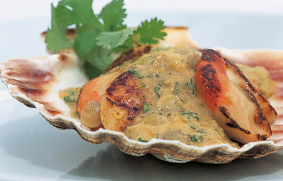 a pictur eof cooked scallops in a shell with lentils sauce and parsely garnish on the top