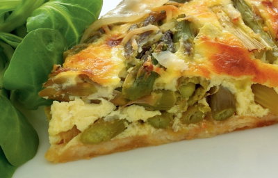 a picture of a slice of asparagus tart with salad leaves on a white plate