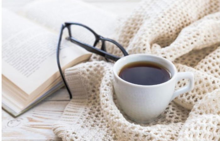 a picture of a cup of coffee, reading glasses and an open book