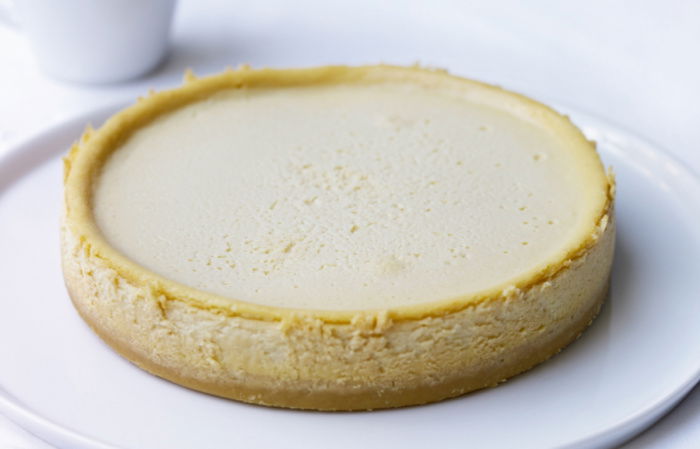 A picture of a vanilla cheesecake on a white plate with a white jug of caramel sauce next to it