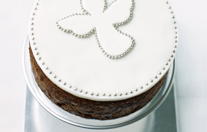 a picture of a cooked cake on a silver cake board, with white icing and an angel marked out in little silver balls
