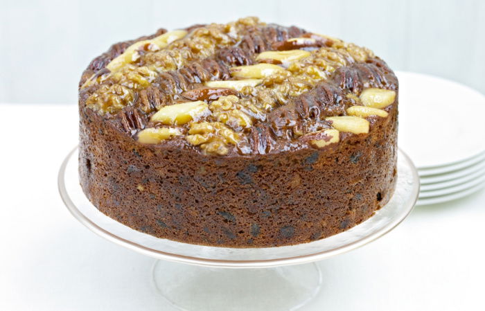 A picture of a fruit cake decorated with nuts on the top on a white cake stand