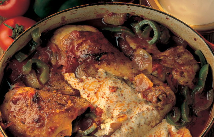 A round oven dish of cooked chicken paprika with green peppers and soured cream on the top