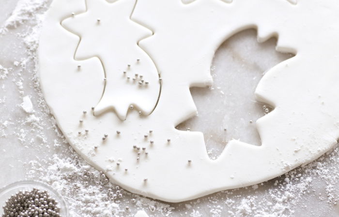 a picture of a circular sheet of white fondant icing on a white surface. three shooting stars have been cut out, a little dish of silver balls alongside and icing sugar on the top