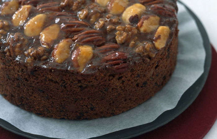 A picture of a round fruit cake decorated with nuts on the top on a dark plate
