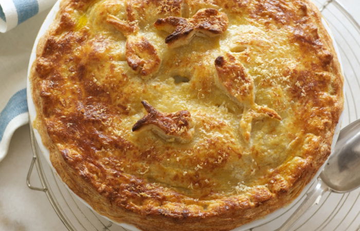 picture of Delia Smith recipe for luxury seafood pie with a parmesan crust served in white dish on wire rack with a serving spoon