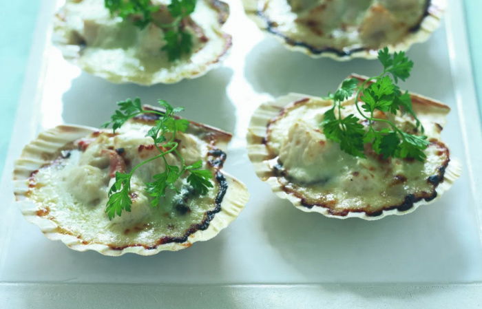 A picture of four scallops in their shells sitting on a white plate