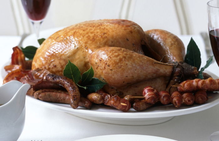 a picture of a table set with white plates, cutlery wine glasses and a cooked turkey with all the trimmings