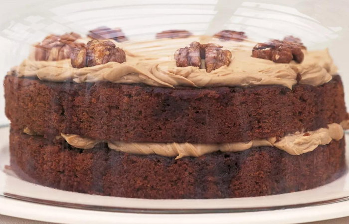 A picture of a layered cake with frosting and walnuts on top, displayed under a glass dome.