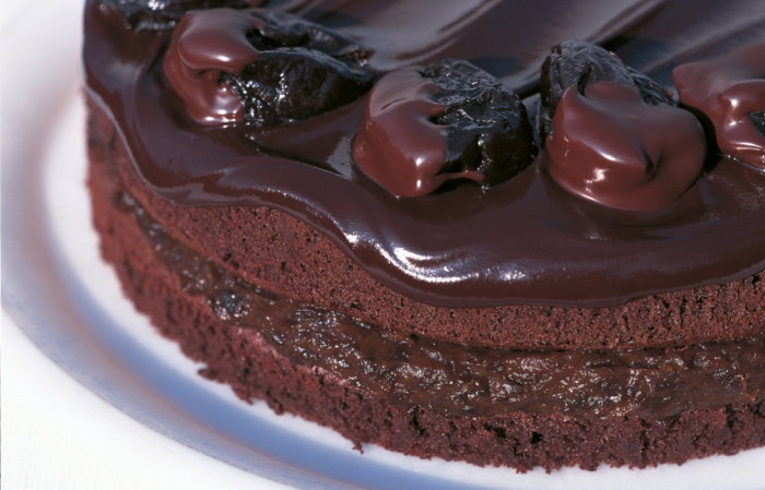 a picture of a round chocolate sponge cake on a white plate with chocolate covered prunes decorating the top