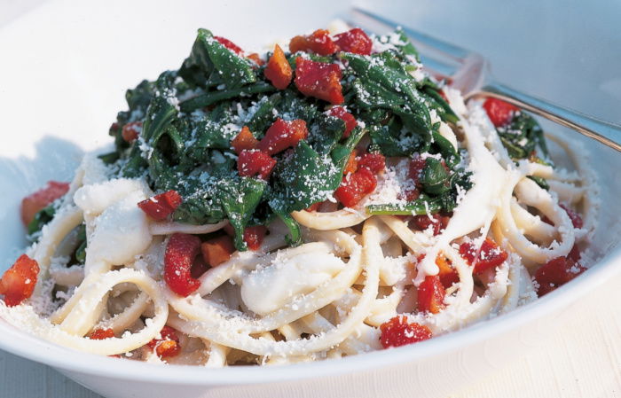 a white bowl of linguine with a gorgonzola sauce, cubes of mozarella, spinach, bacon and parmesan on top 