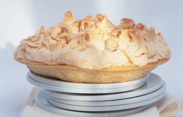 six white plates with a cooked lemon meringe pie balanced on the top