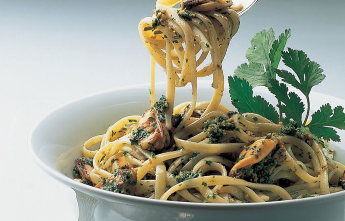 a blue bowl filled with linguine pasta with mussels and walnut parsley pesto