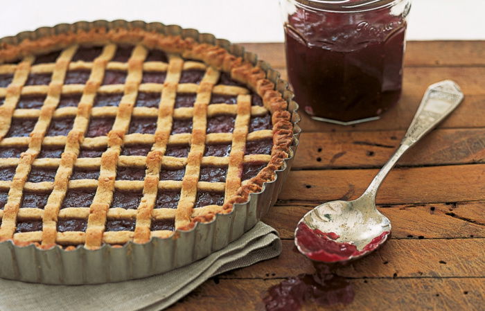 a picture of a linzertorte tarte in a flan tin with latticed pastry across the top and a jar of jam and spoon next to it