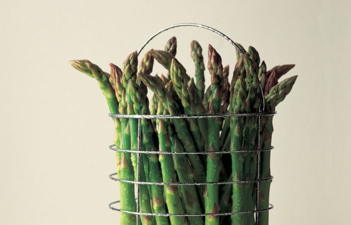 a picture of fresh asparagus in a wire container sitting on a marble surface