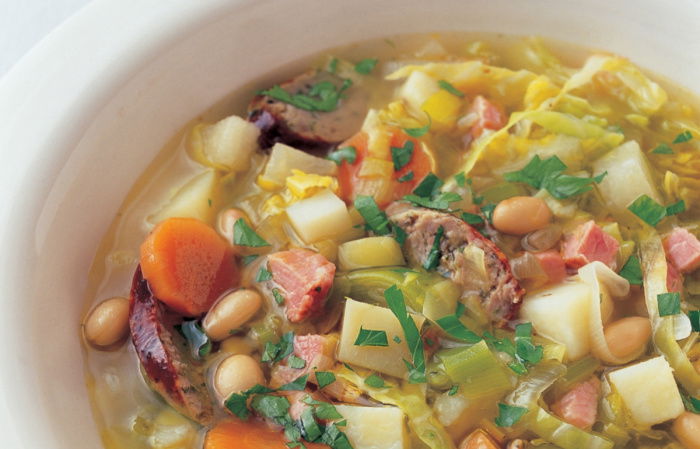 A white bowl of soup showing diced vegetables and frankfurter