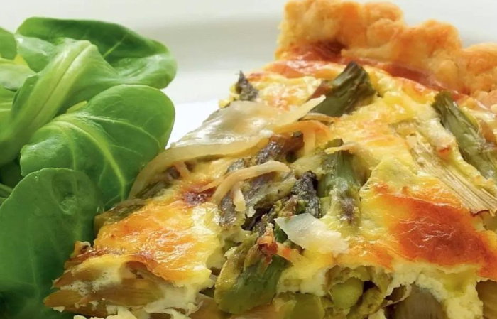 a picture of a slice of asparagus tart with salad leaves on a white plate