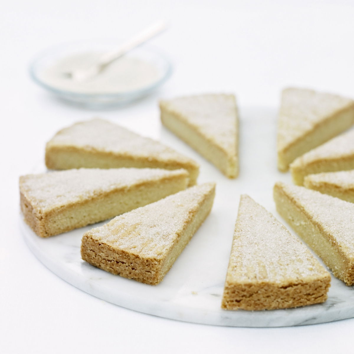 Eight slices of shortbread dusted with sugar on a whilte marble plate