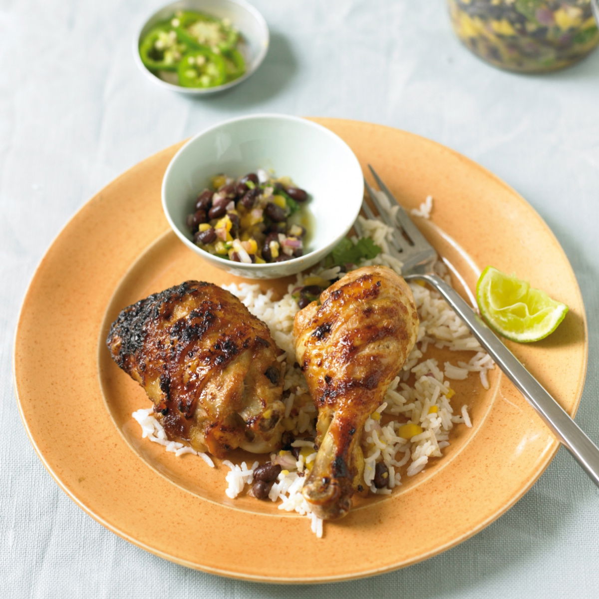 a yellow plate of cooked chicken and rice with a wedge of lemon on the edge