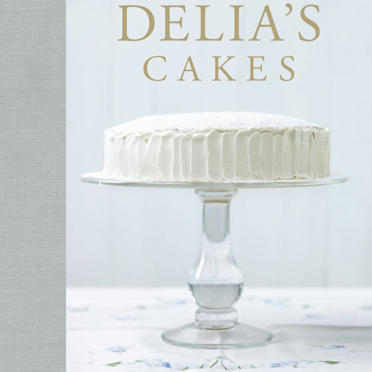 The cover of the book Delia's Cakes showing a white cake on a pretty glass cake stand