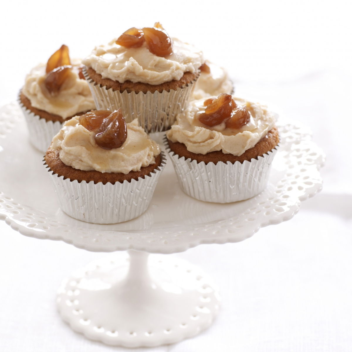a pretty white cake stand with four chestnut cupcakes in silver muffin cases