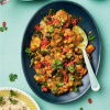 a colourful picture of a black dish with chickpea curry garnished with coriander, and a dish of cooked rice next to it