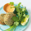 a picture of two cooked crab cakes on a blue plate with a little dish of sauce on the side and a garnish of parsley and lemon wedge