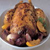 A picture of a roasted chicken in a dish surrounded by lemon wedges, thyme and garlic