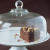 A slice of chocolate cake on a white cake stand with a glass lid